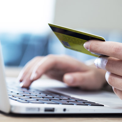Image of one hand holding a credit card and another typing on a laptop