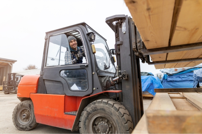 A person lifting some lumber with a forklift